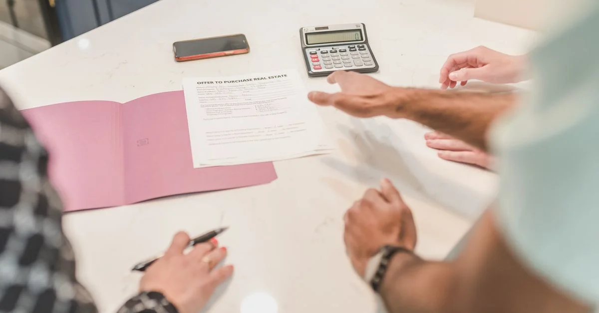 Mains gesticulant lors d'un examen de documents immobiliers sur un bureau moderne avec une calculatrice.