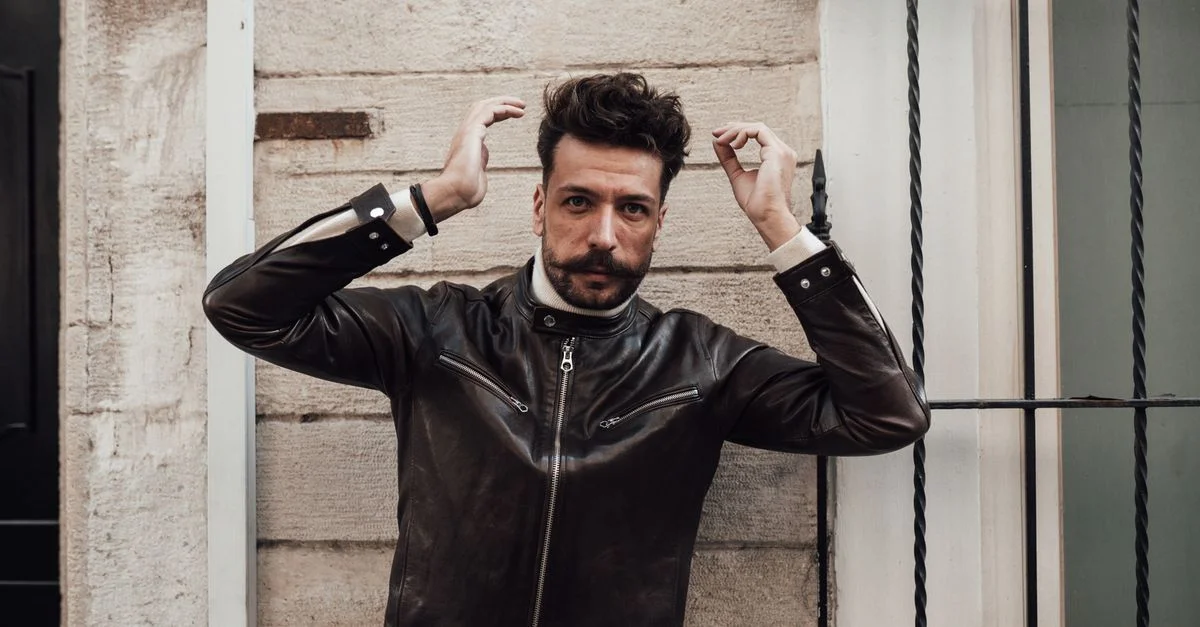 Jeune homme charismatique en cuir pose avec confiance sur un fond urbain.