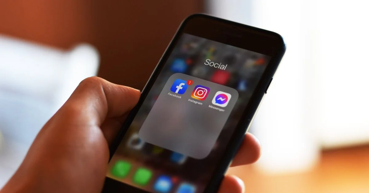 Gros plan sur une main tenant un smartphone montrant des applications de réseaux sociaux telles que Facebook et Instagram.