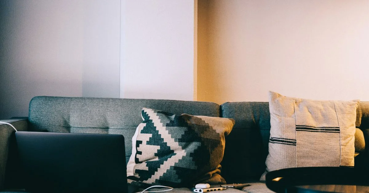 Un aménagement de salon confortable avec un canapé, des coussins et un ordinateur portable, idéal pour la détente et le travail à distance.