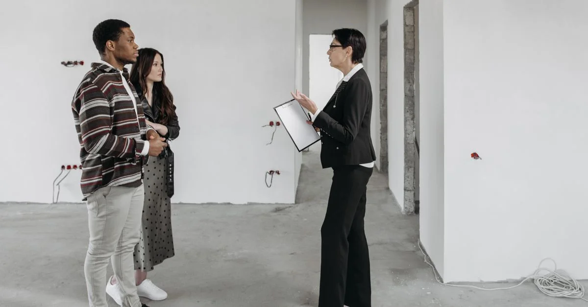 Agent immobilier montrant une maison à un couple dans un intérieur de maison récemment construit.