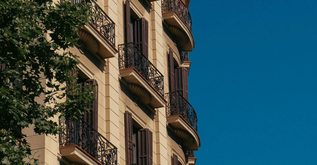 Charmante façade de bâtiment à Barcelone avec des balcons intricats sous un ciel d'été dégagé.