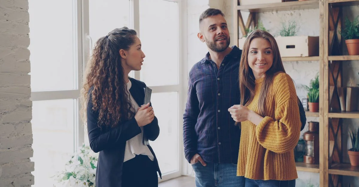 Agent immobilier présentant un appartement à un couple souriant dans un cadre moderne et confortable.