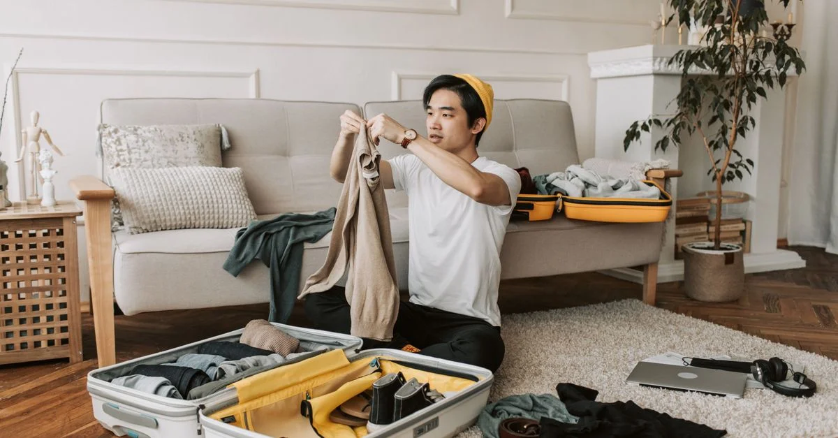 Un jeune homme organise des vêtements dans une valise dans un salon élégant, se préparant pour un voyage.